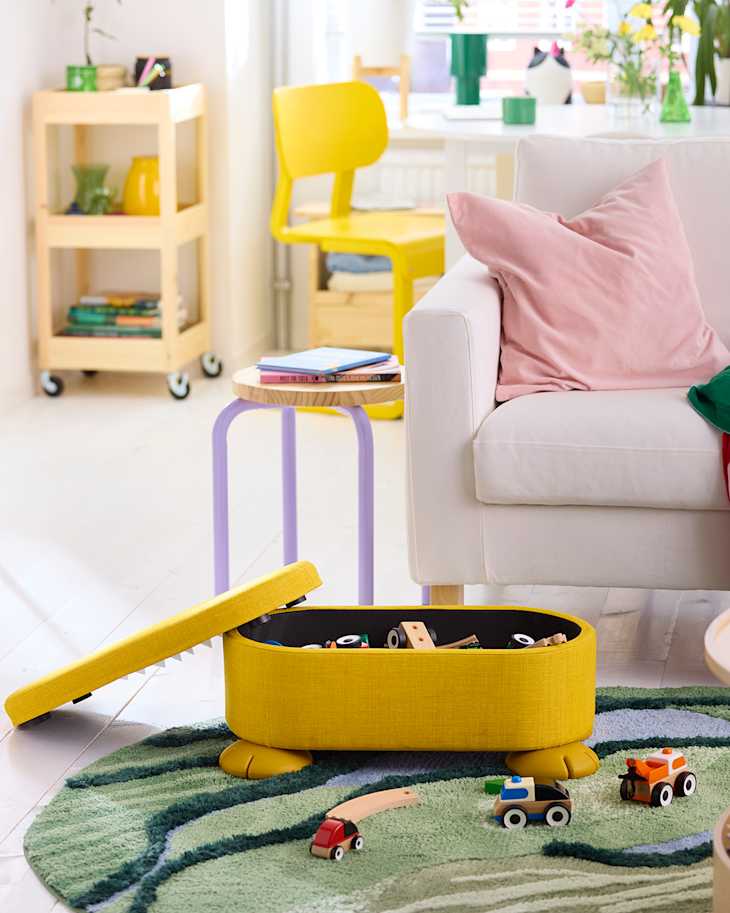 Bright living room with a yellow storage box, colorful toys, a white sofa, and a green rug.