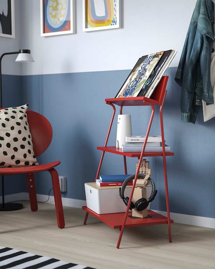 Cozy corner with a red chair and a red shelving unit holding books, headphones, and decor, against a blue wall.