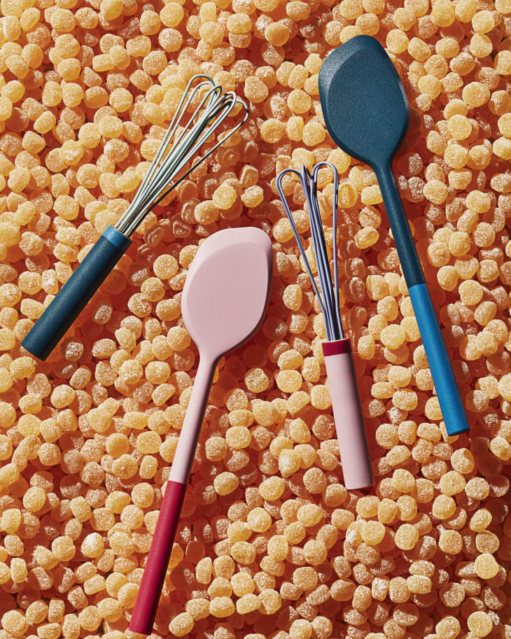Colorful kitchen utensils on a bed of orange gummy candies.