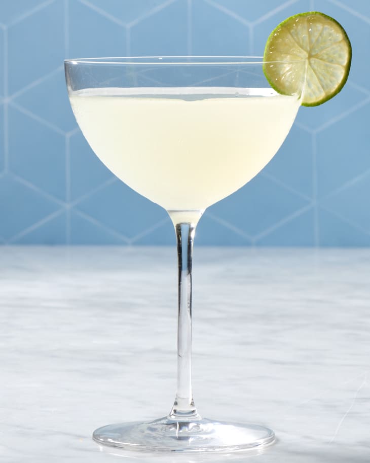 a classic daiquiri cocktail in a coupe glass with a lime garnish against a blue backdrop