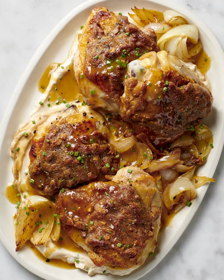 a platter with cooked chicken thighs resting on a bed of french onion dip and cooked onions