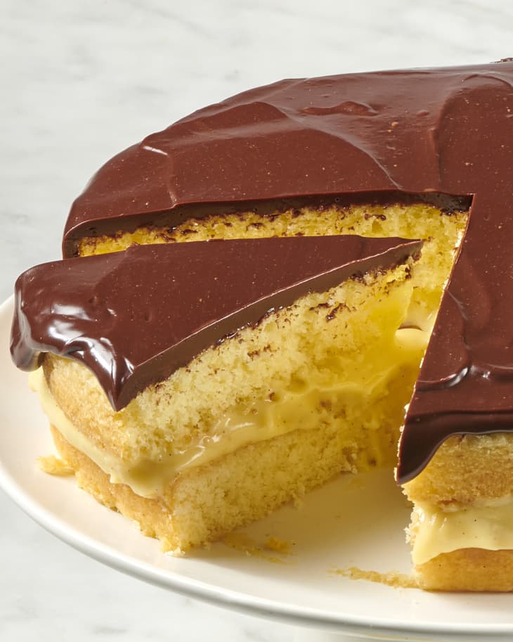 a boston cream pie on a cake stand with a slice missing and a second one separated from the rest of the cake