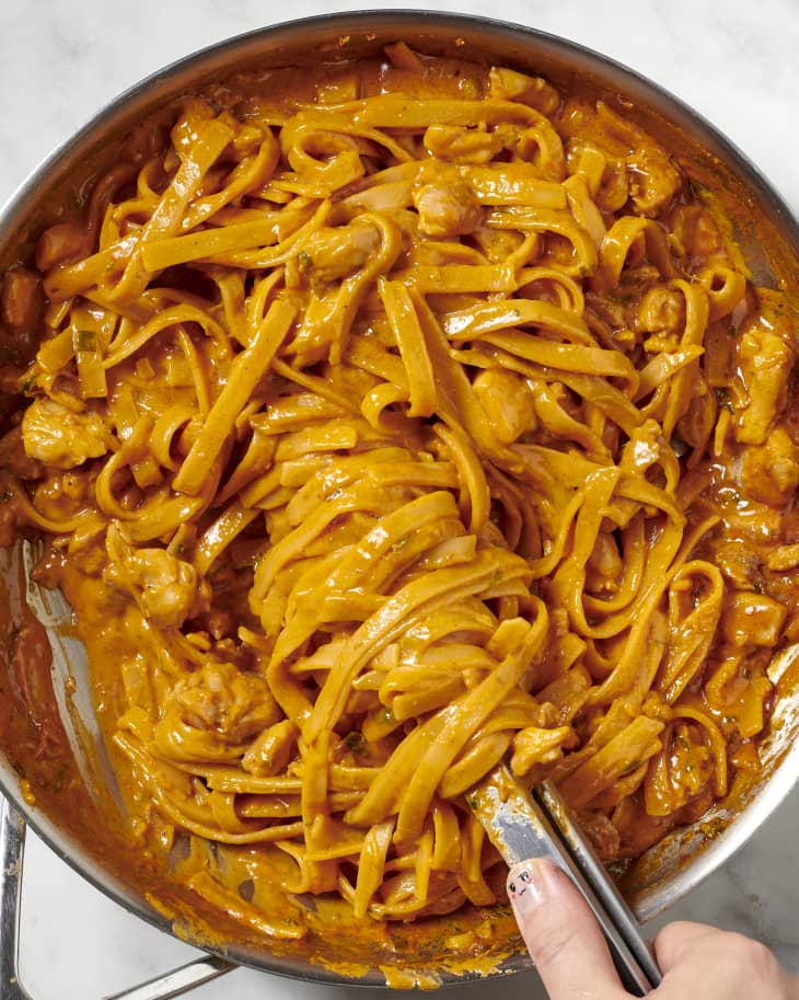 gochujang chicken alfredo pasta in a skillet with some twirled around a pair of tongs for serving