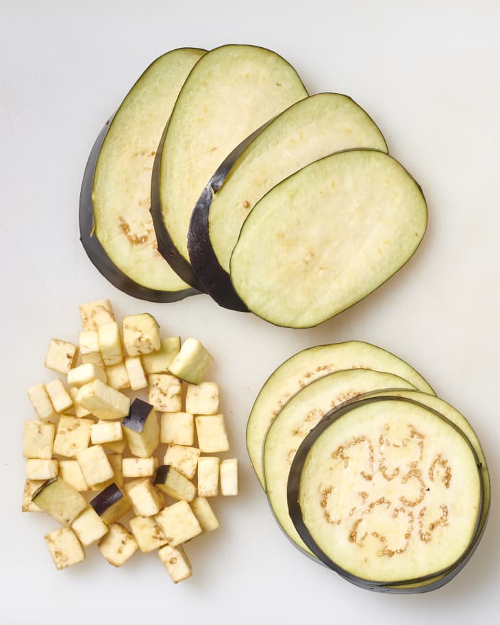 eggplant cut in ovals, rounds, and cubes on a white cutting board