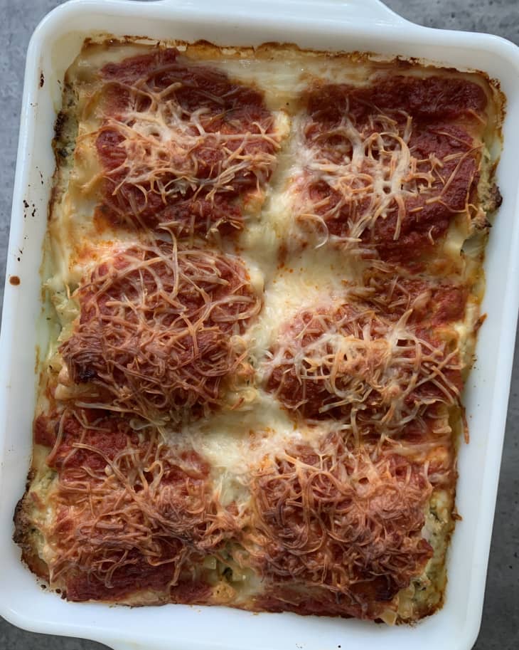 Baked lasagna in a white dish topped with melted cheese and tomato sauce.