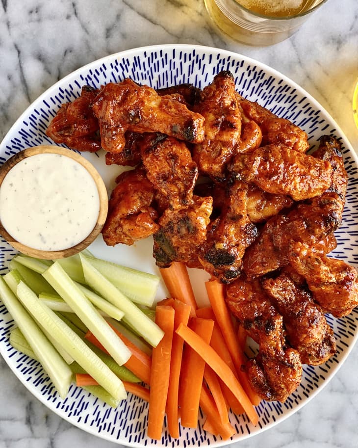 Photograph of grilled chicken wings covered in buffalo sauce on a serving plate with carrot sticks, celery sticks, and blue cheese dressing.