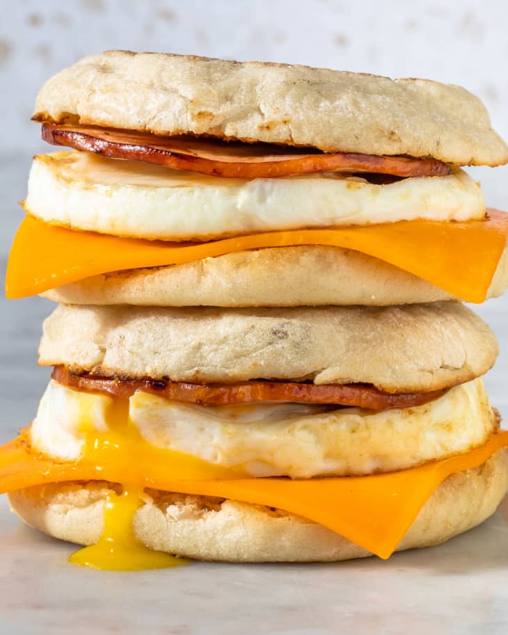 two egg muffin sandwiches stacked on top of each other placed on marble surface with egg yolk falling on side of sandwich