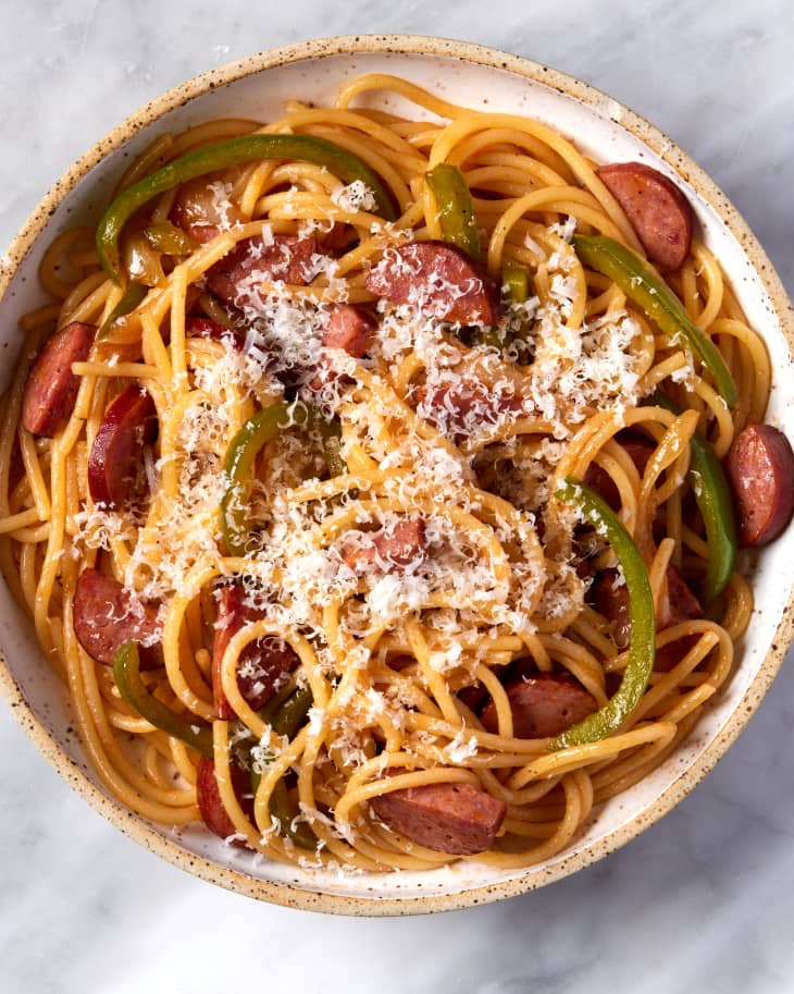 close up overhead shot of bowl with napolitan spaghetti, bell peppers, and sausage with cheese sprinkled on top on a marble surface
