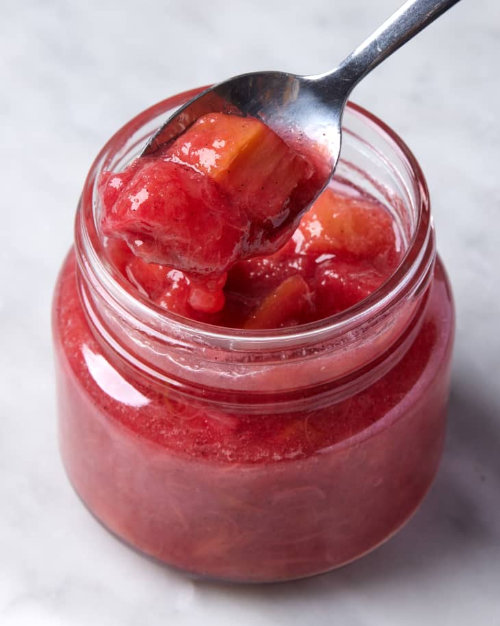 jar of rhubarb compote on marble surface with a silver spoon scooping some out