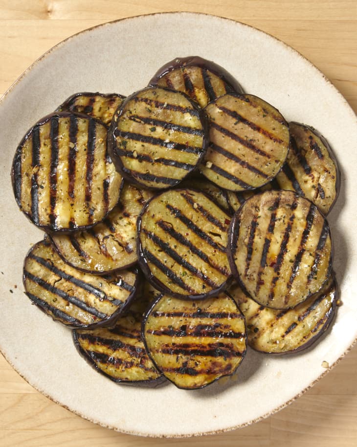 overhead shot of grilled eggplant on white plate that's placed on a wooden surface