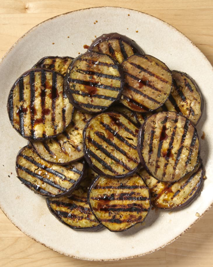 overhead shot of grilled eggplant with sauce on white plate that's placed on a wooden surface
