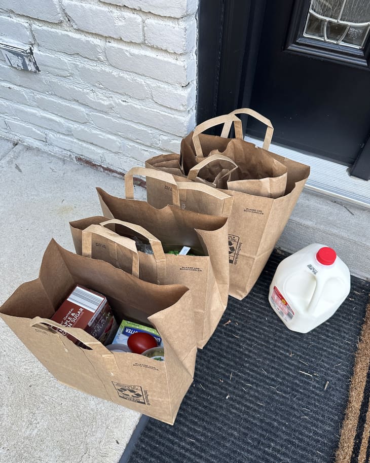 Paper grocery bags full of groceries and a plastic carton of milk on a front doorstep
