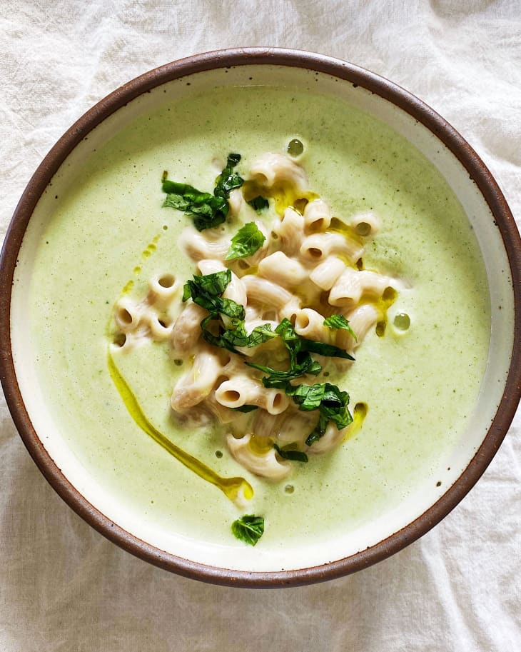 creamy broccoli soup sits in a white bowl with noodles peeking through the surface