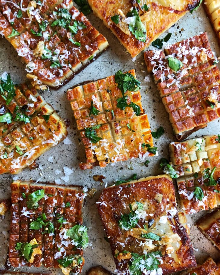 Crispy waffle fries topped with grated cheese and fresh herbs on a baking sheet.
