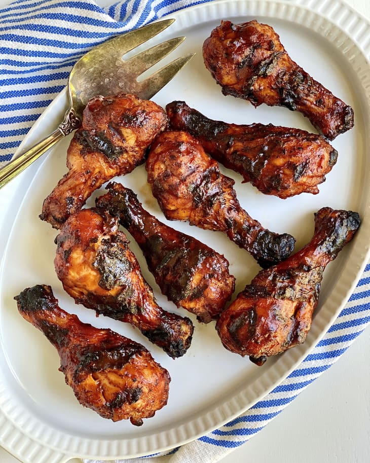 Photograph of grilled chicken drumsticks on a serving plate and striped kitchen towel.