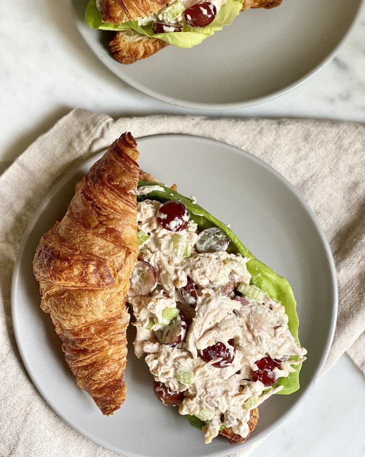 Croissant filled with chicken salad, grapes, and lettuce on a gray plate.