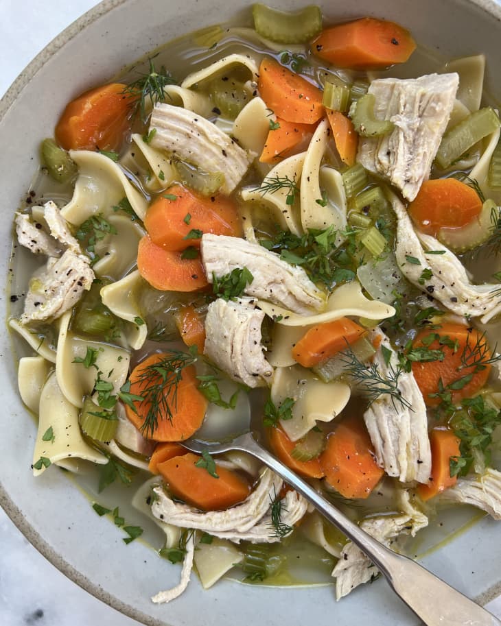 Photograph of turkey noodle soup in a bowl with a silver spoon.