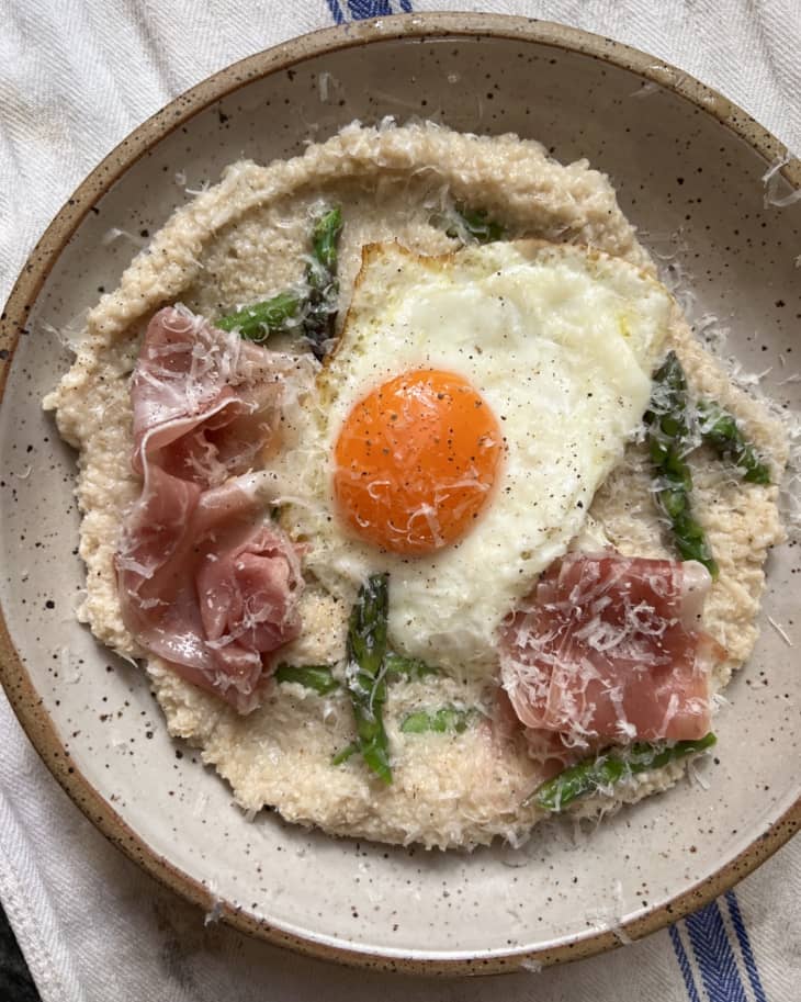 Fried sunnyside up egg over cooked oat bran with prosciutto and asparagus