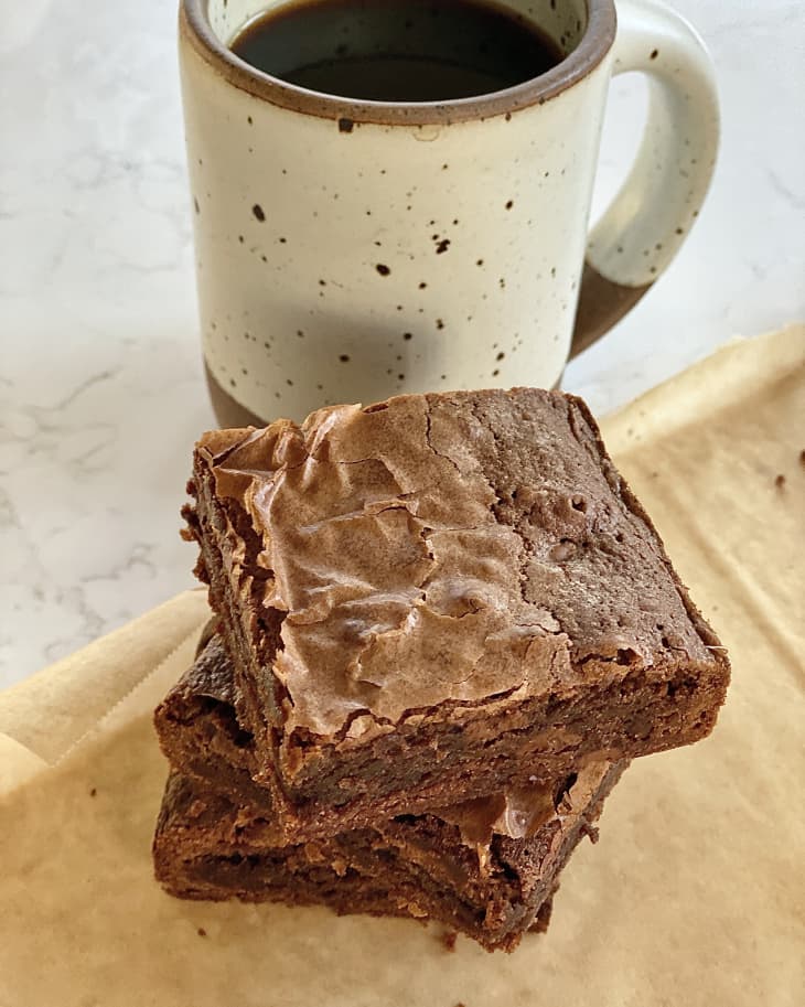 Coffee brownie stacked on wax paper with cup of coffee beside.