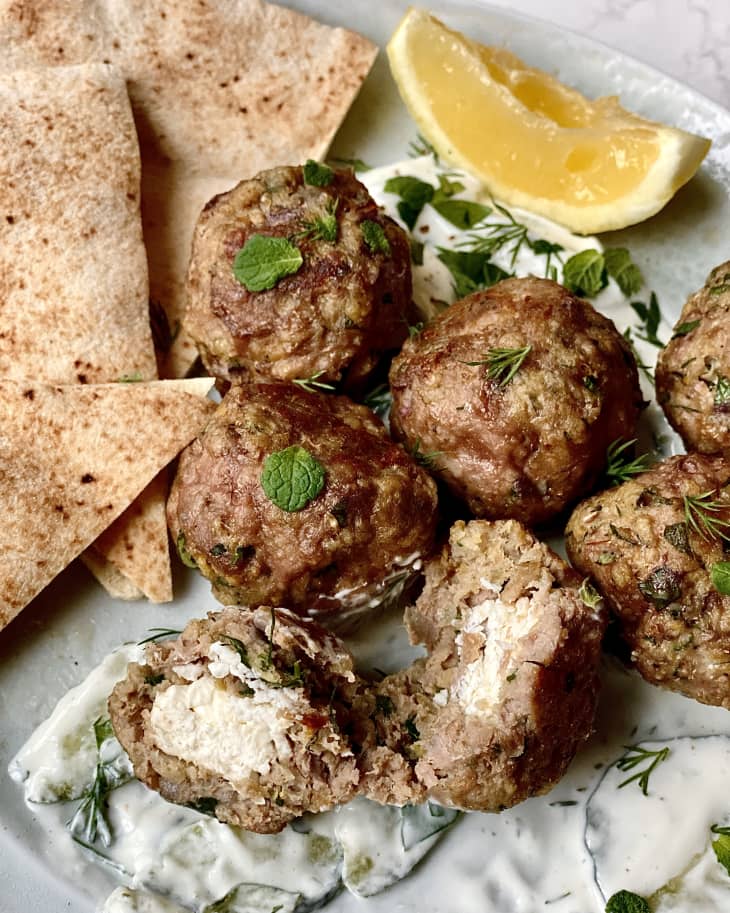 Lamb meatballs on plate with creamy sauce, herbs and pita. With one meatball broken open showing feta filling.