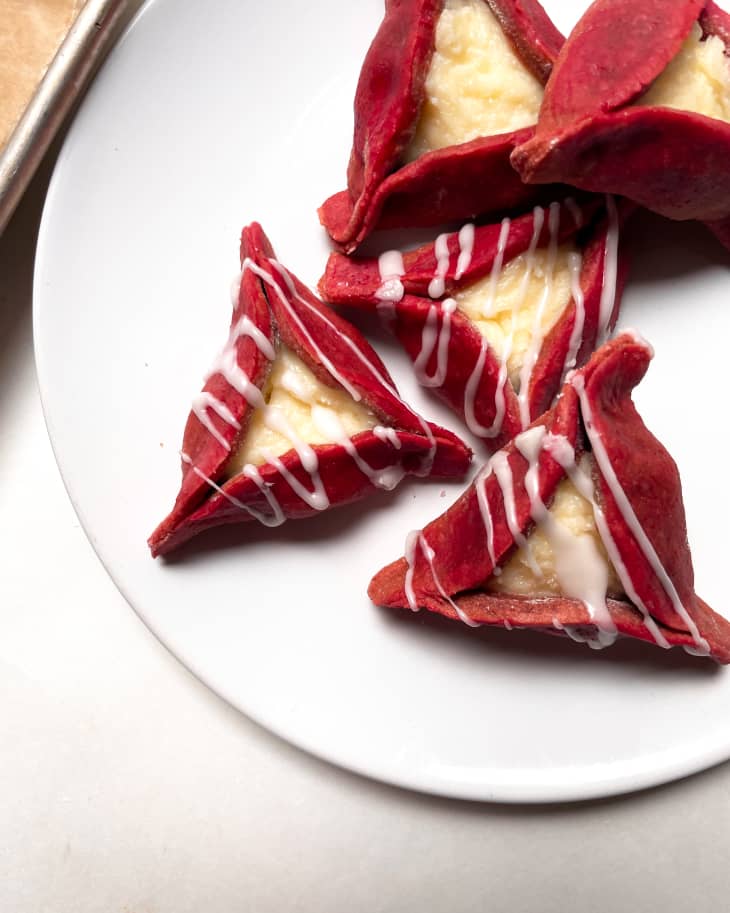 Red velvet hamantaschen on a plate; some drizzled with icing some without icing.