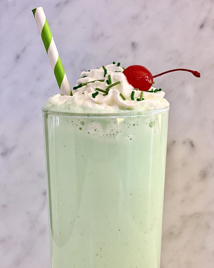 Shamrock shake topped with whipped cream and green sprinkles with a green and white straw in the glass.