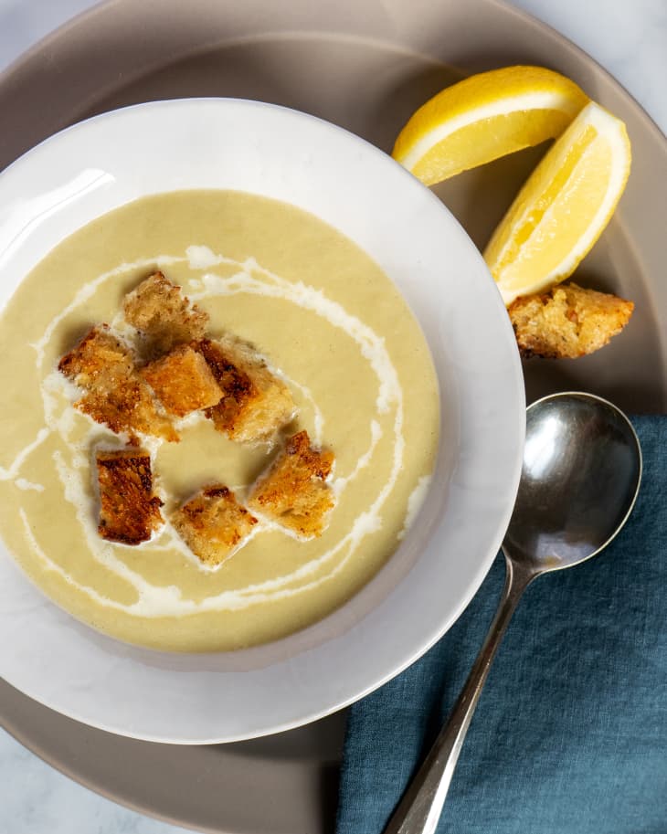 Cream of Artichoke Soup in bowl with croutons and lemons. Blue cloth napkin, lemon wedges, and spoon