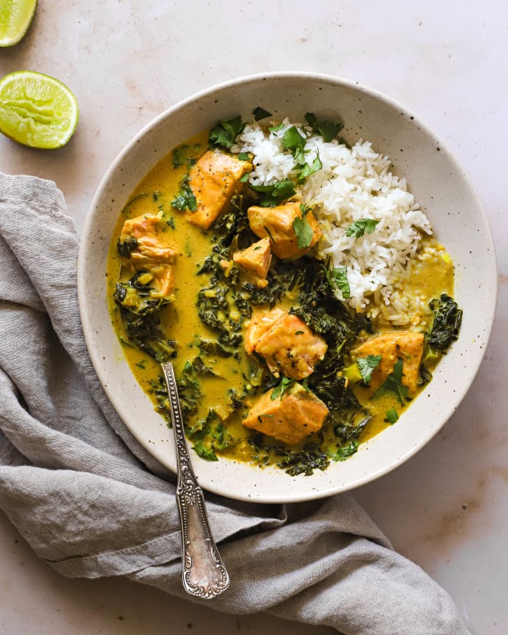 Kale and salmon coconut curry served in a bowl with rice, limes off to the side.