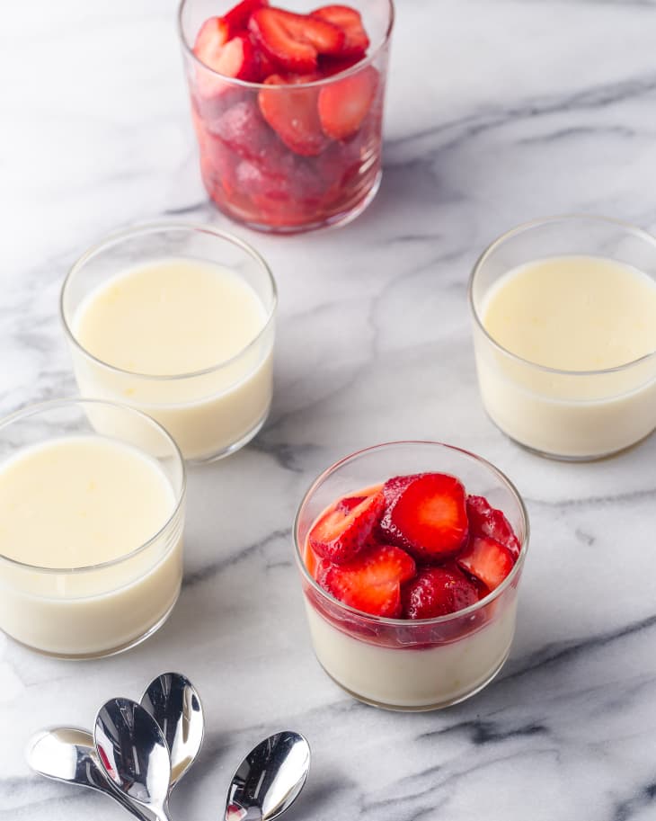 Lemon posset in glass cups with strawberries on the top and spoons off to the side.