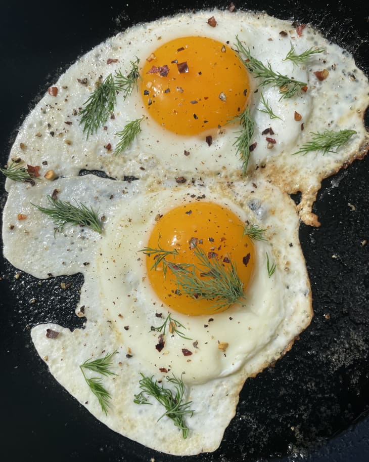 Pickle brine fried egg in skillet garnished with dill and red pepper flakes.