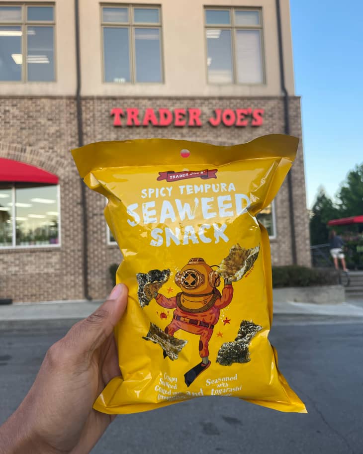 Someone holding up bag of Trader Joe's seaweed snacks in front of Trader Joes.