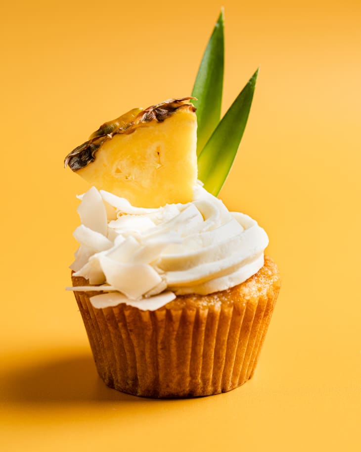 Pina colada cupcake with pineapple wedge garnish on yellow background.