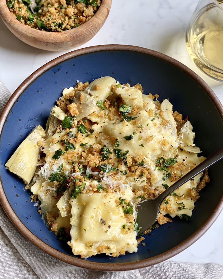 Overhead photo of Ravioli with Artichokes and Garlic Breadcrumbs in a blue bowl with extra breadcrumbs and a glass of wine