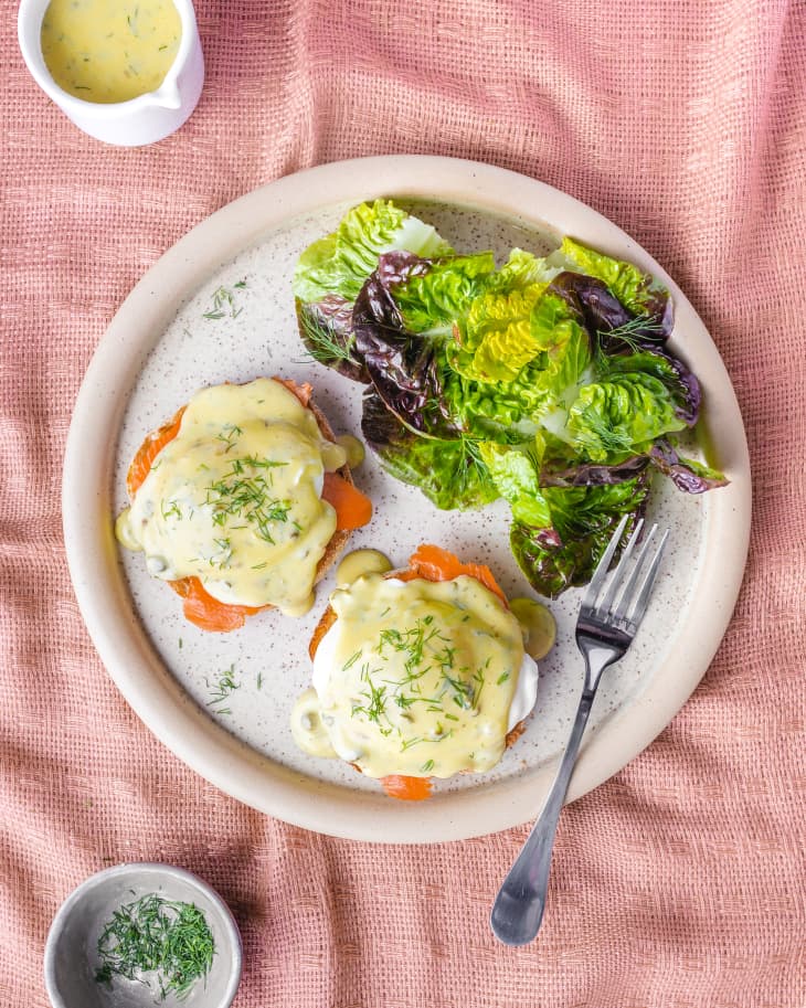 Smoked salmon eggs benedict on a plate with small salad on the side.