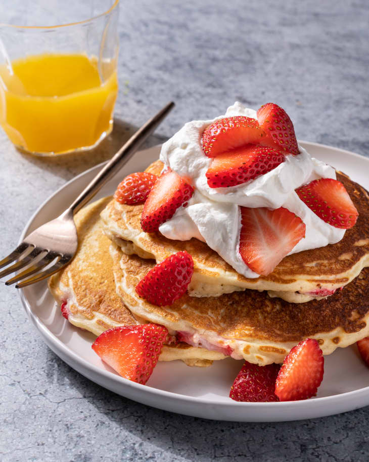 Strawberry pancakes on a plate with side of orange juice.
