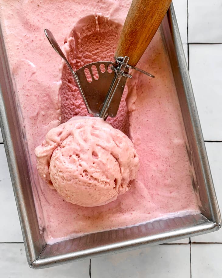 An ice cream scooper scooping out strawberry ice cream