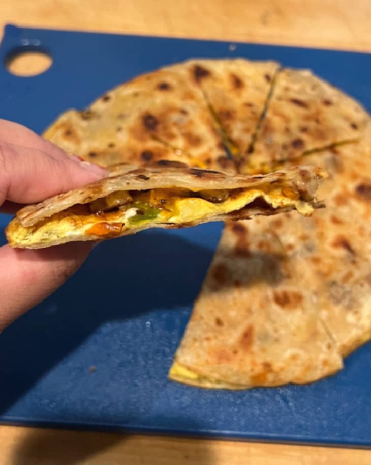A hand holding a triangle of a breakfast quesadilla
