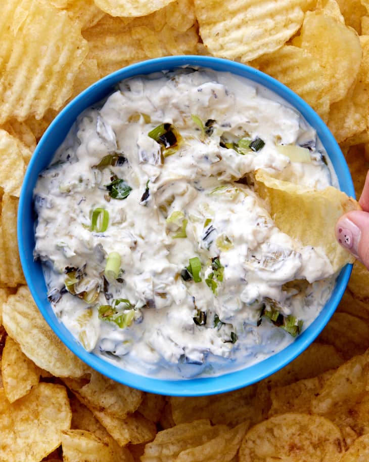 Someone dipping potato chip into sour cream charred scallion dip.