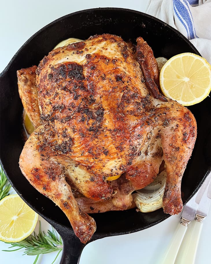 Roasted chicken in skillet with lemon halves on the side.