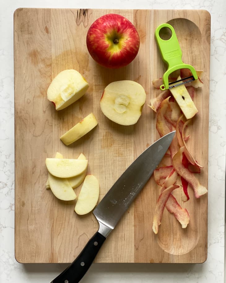 A peeled apple and knife on a wooden cutting board