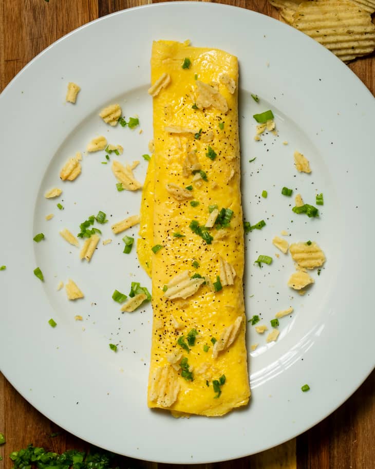 French omelet on plate garnished with potato chips and parsley.