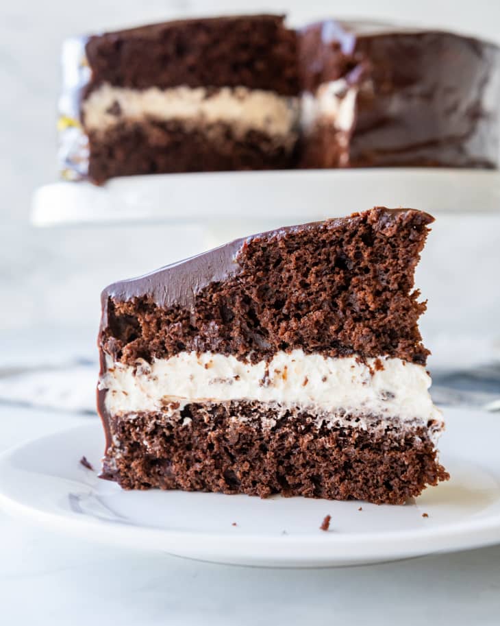 slice of chocolate cake with large cream filling on a plate with cake in the background