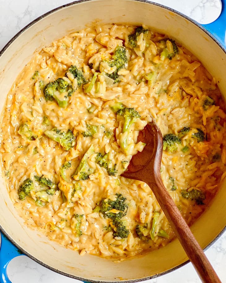 Broccoli cheddar orzo in Dutch oven with wooden spoon.