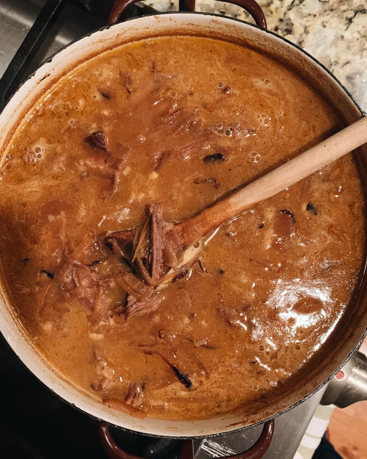 Beef stew simmering in a pot with a wooden spoon on a stovetop.