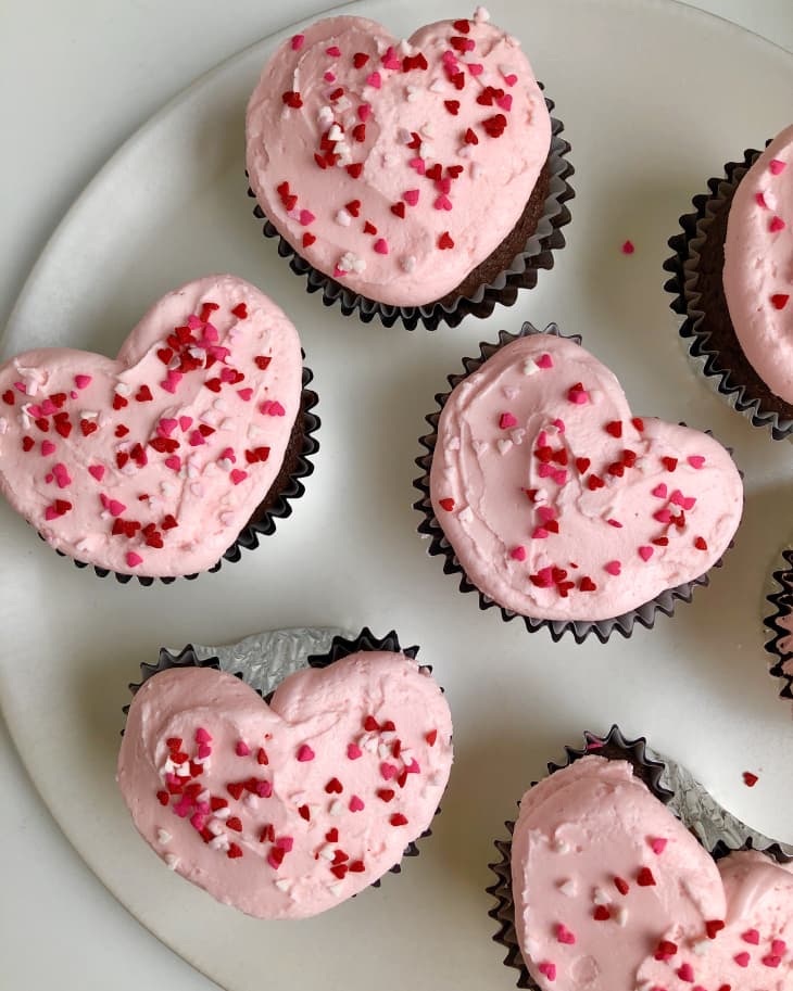 Heart-shaped cupcakes with pink frosting and red sprinkles on a white plate.