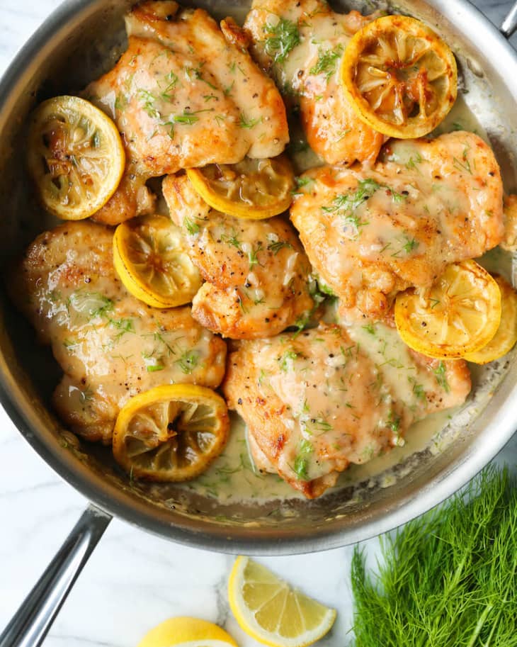 Chicken thighs in a skillet with lemon slices and fresh dill.