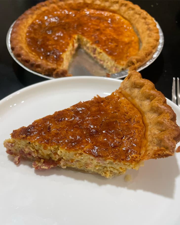 Slice of cowboy quiche on plate with remaining quiche in background.