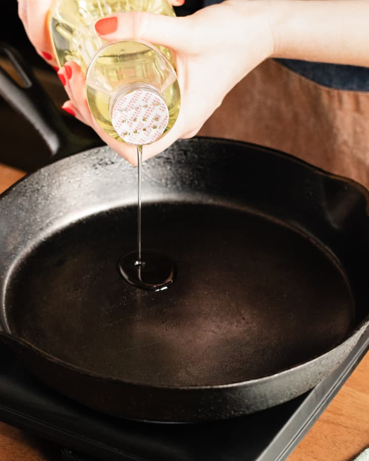Someone pouring vegetable oil into cast iron skillet