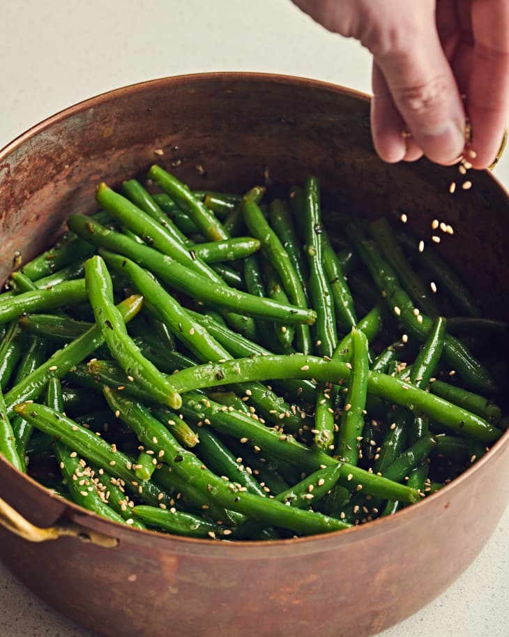 Sauteed green beans in bowl being sprinkled with sesame (benne) seeds