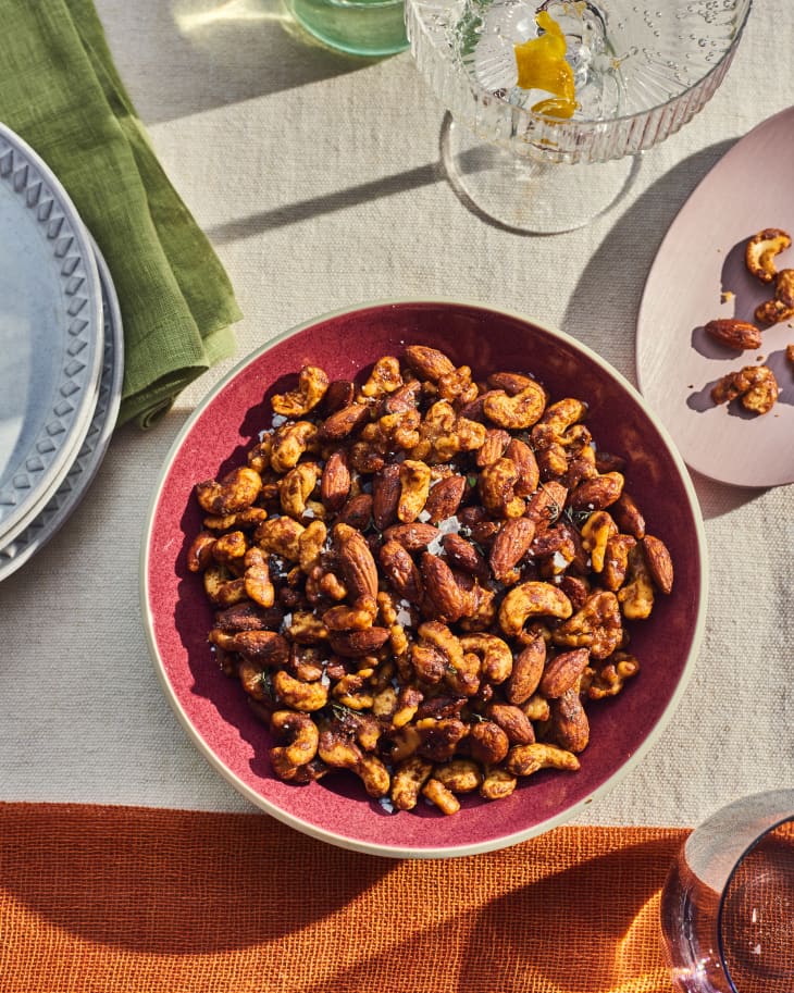 Bowl of candied nuts on table. cocktail with a twist in the background. Plates and napkins around